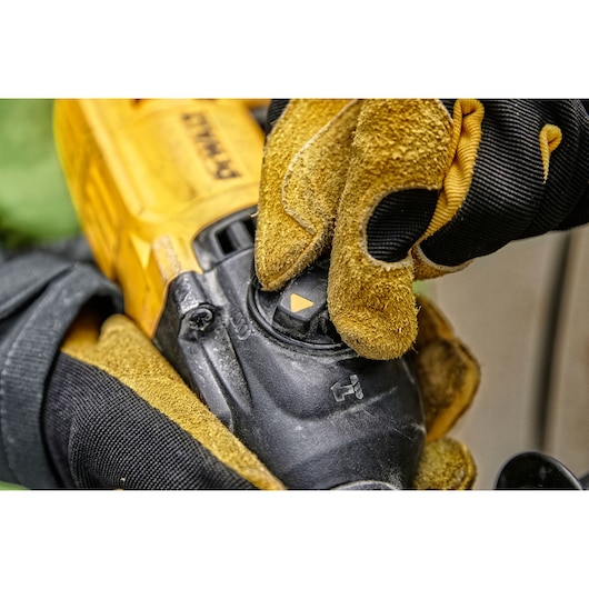 Close-up of a person wearing yellow and black work gloves adjusting the mode selector on a DEWALT power tool.