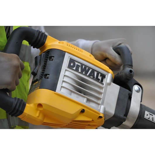 Close-up image of a person holding a yellow and black DEWALT demolition hammer, wearing gloves and a safety vest.