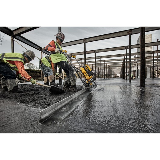 Workers use a DEWALT power tool to smooth wet concrete in a large building construction site.