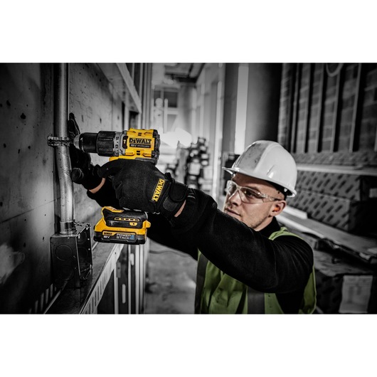 Worker uses DEWALT Powerstack battery in a cordless drill during electrical installation on an industrial site.