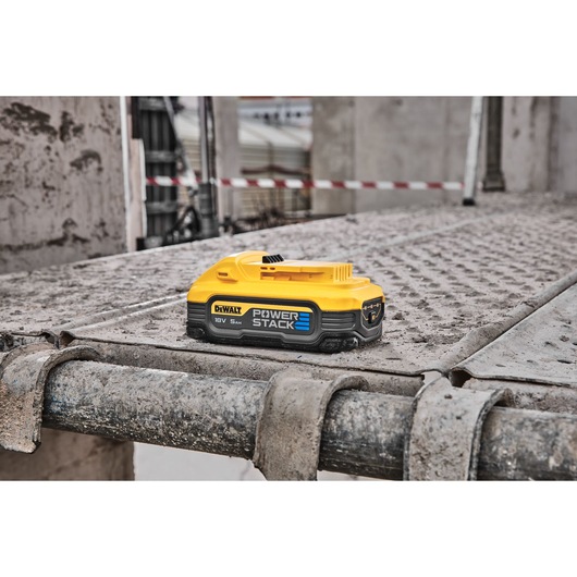DEWALT POWERSTACK DCBP518 battery on a dusty construction site metal platform.