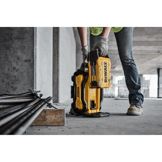 Person uses a yellow DEWALT battery pack on a construction site with tools and metal bars nearby.