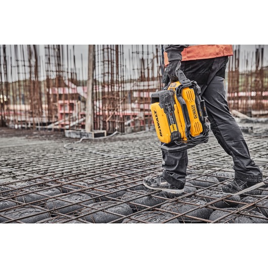 Person walking on construction site holding a DEWALT tool case.