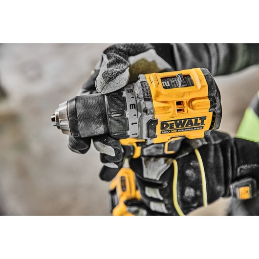 Close-up of a gloved hand holding and using a yellow and black DEWALT 18V XR brushless cordless drill.
