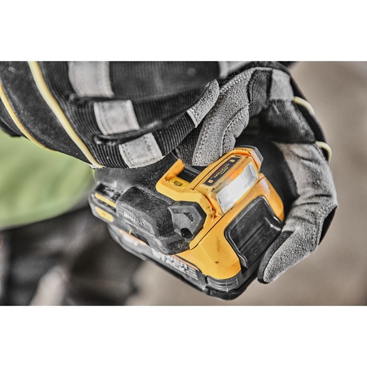 Close-up of a gloved hand holding a yellow and black DEWALT power tool with a lit LED work light.