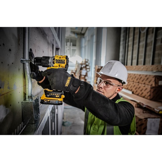 Worker uses a DEWALT DCD805E2T drill on a metal pipe in a construction site while wearing safety gear.