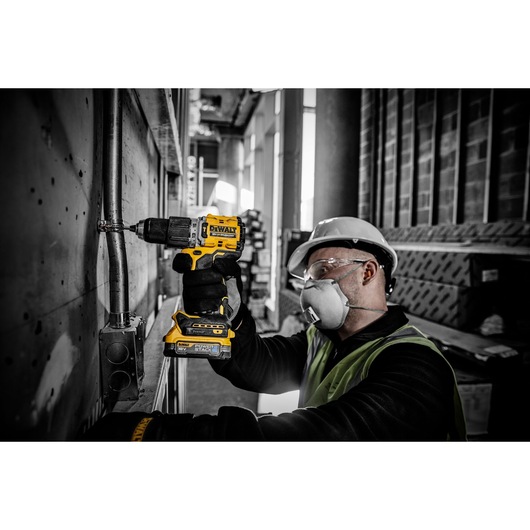 Person using DEWALT DCD805E2T drill on metal pipe at construction site, wearing safety gear.