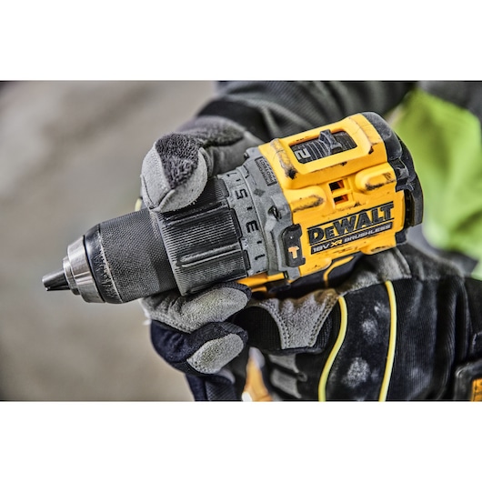 Close-up of a person wearing work gloves holding a yellow and black DEWALT 18V XR brushless cordless drill.