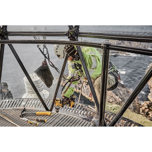 DEWALT DCD996P2, DCD996P2-QW tools used outdoors on a metal structure by a worker in safety gear.
