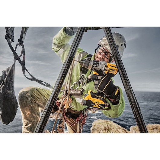 DEWALT DCD996P2, DCD996P2-QW drill used outdoors by worker; sea and rocks in background. Photography category.