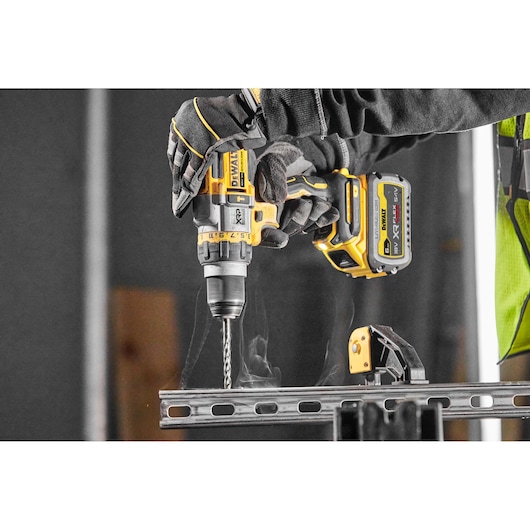 DEWALT cordless drill in use on metal, worker wearing gloves, close-up of tool and battery.