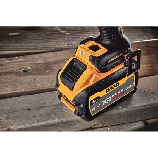 Close-up of a DEWALT XR FLEXVOLT 18V/54V battery attached to a tool resting on wooden planks.