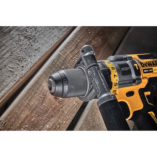 DEWALT DCD999T1 cordless drill in use on wood, yellow and black design with side handle and sawdust visible.