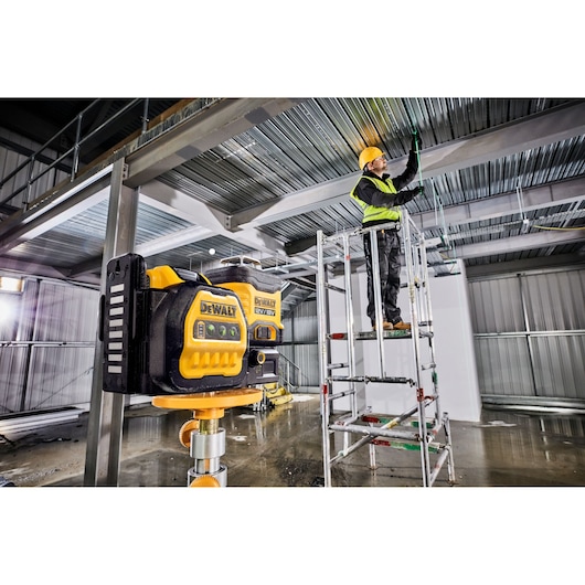 DEWALT laser level used at a construction site, worker adjusts ceiling wiring on a scaffold.