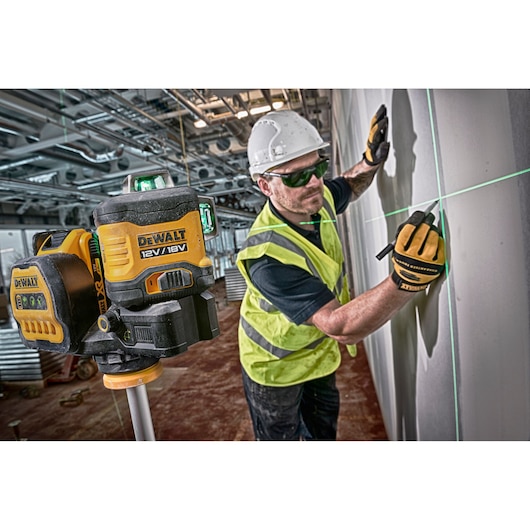 DEWALT laser level used by a worker in a vest and helmet marking lines on a wall at a construction site.