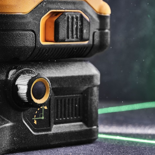 Close-up of a DEWALT laser level adjustment knob and green laser line on a dark surface.