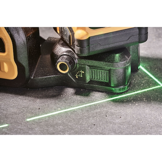 Close-up of a DEWALT laser level tool projecting green lines on a gray surface.