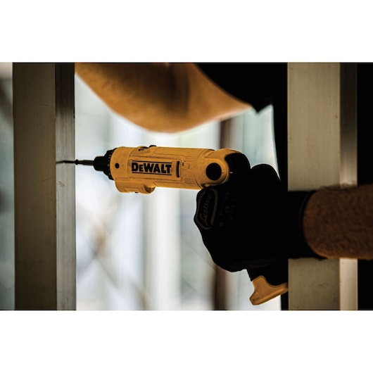 A person using a DEWALT yellow cordless screwdriver to drill into a metal frame, wearing protective gloves.