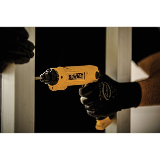 A person wearing black gloves using a yellow DEWALT electric screwdriver to drive a screw into a metal frame.
