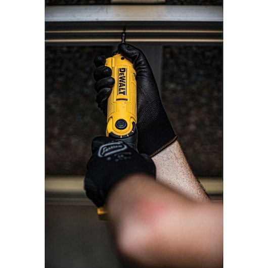 A person wearing black work gloves uses a yellow DEWALT cordless screwdriver to drive a screw into a metal frame.