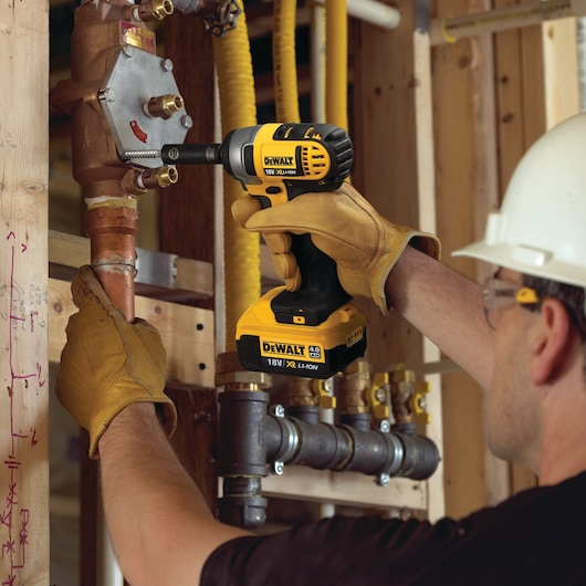 Worker uses DEWALT DCF880M2 cordless impact wrench on plumbing pipes at construction site.