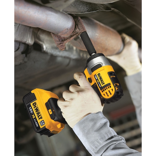 Person uses DEWALT 18V cordless impact wrench on a rusty pipe, wearing gloves and work clothes.