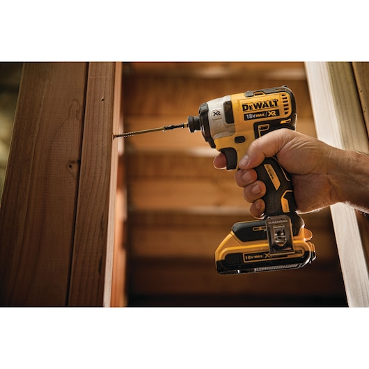 A hand holding a DEWALT 18V cordless impact driver while drilling a screw into a wooden beam.