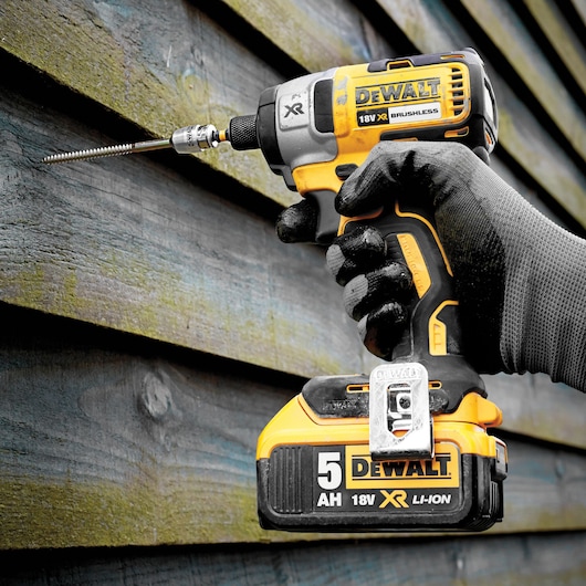 DEWALT 18V XR impact driver being used to drive a screw into a wooden wall by a gloved hand.