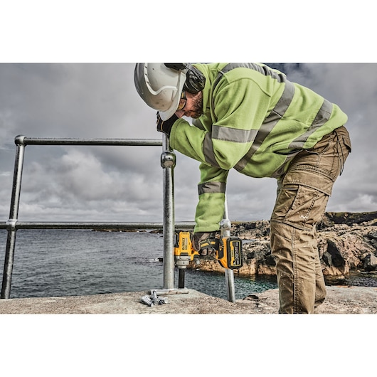 Worker uses a DEWALT power tool outdoors near water, installing metal railings on a stone surface.