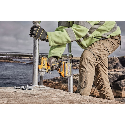 Person uses DEWALT cordless impact wrench DCF894P2 to secure bolts outdoors near water.