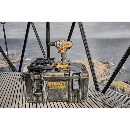 DEWALT drill and ToughSystem 2.0 tool case are displayed on a platform overlooking a rocky coastline.