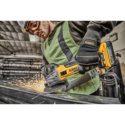 Worker uses DEWALT cordless grinder, producing sparks while grinding metal in an industrial environment.