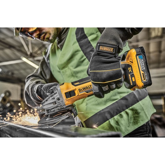 Person using a DEWALT cordless grinder on metal, sparks flying, in a workshop setting.