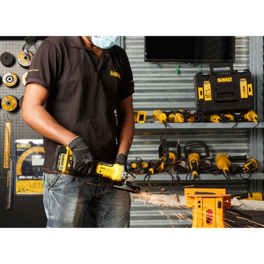 Worker using a grinder on a construction site near water with city skyline in the background.