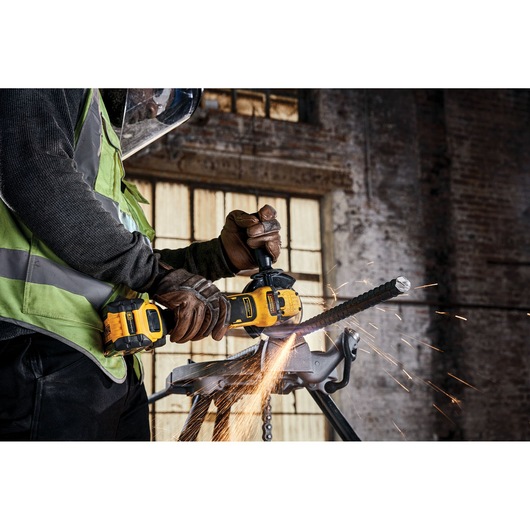 Worker uses DEWALT cordless angle grinder to cut metal rebar, sparks flying at industrial jobsite.