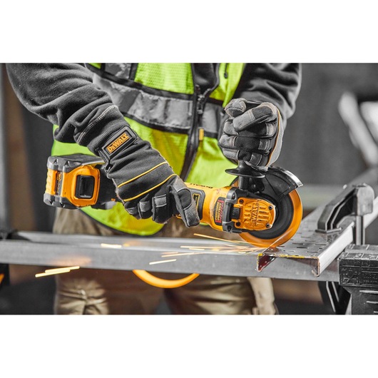 Person uses DEWALT cordless grinder on metal, wearing gloves and safety vest with visible sparks.