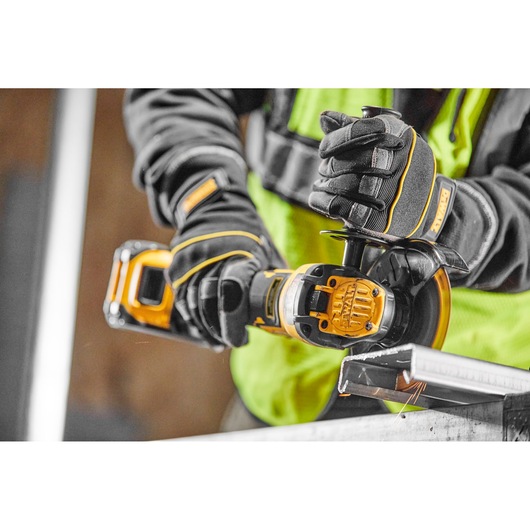 Person using DEWALT cordless angle grinder to cut metal, wearing gloves and safety vest.