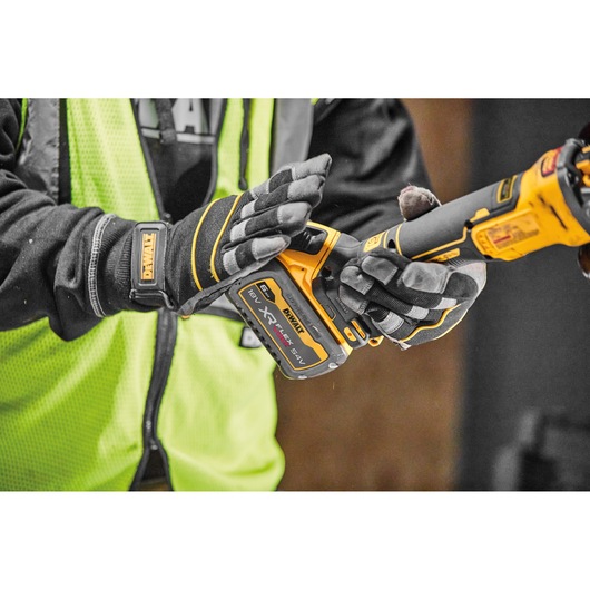 Person with gloves holds a DEWALT cordless XR FLEXVOLT power tool, wearing a yellow safety vest.