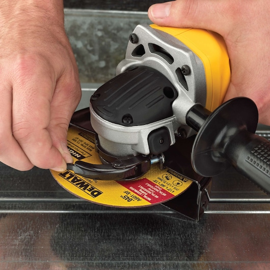 Hands adjusting a DEWALT angle grinder with a yellow grinding disc on a metal surface.