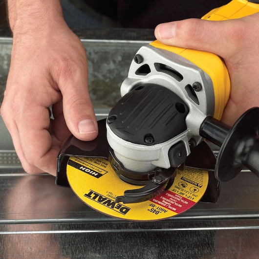 Hands using a yellow DEWALT angle grinder with a metal cutting disc on a metal surface.
