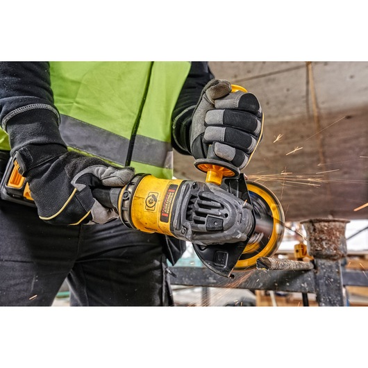 Gloved hands using a DEWALT cordless grinder, cutting metal with visible sparks in a construction setting.