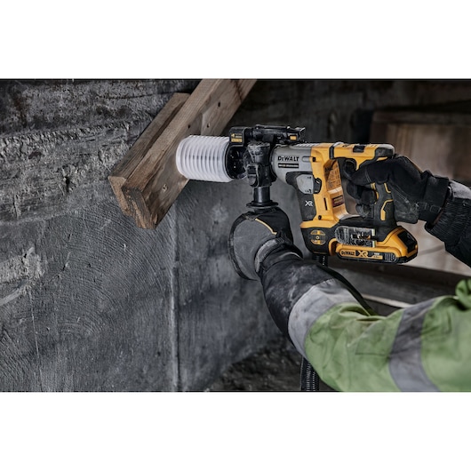 DEWALT cordless hammer drill in use, drilling a hole through wood and concrete by a worker wearing gloves.