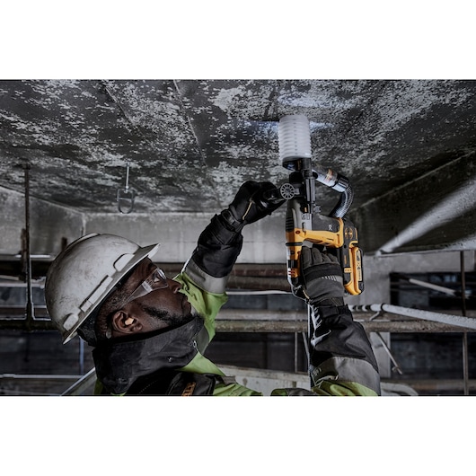 Worker uses a DEWALT DCH172D2 rotary hammer drill with dust extractor to drill into a concrete ceiling.
