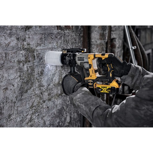 Person using a DEWALT cordless rotary hammer drill to bore into a concrete wall at a construction site.