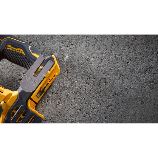 Close-up of a DEWALT brushless yellow power tool resting on a rough concrete surface.