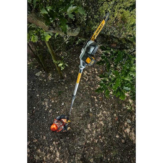 Person using a DEWALT DCMPS567N pole saw to trim high tree branches outdoors.