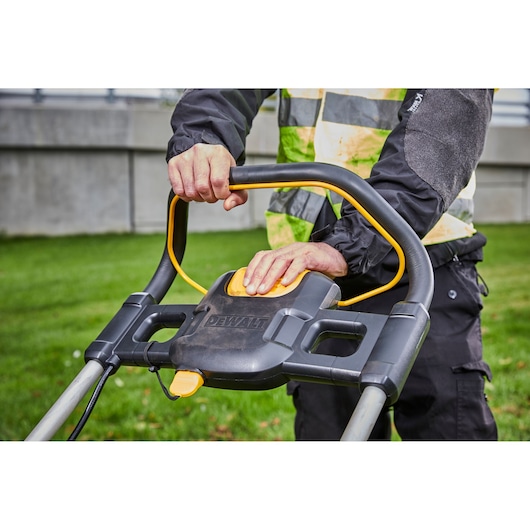 Close-up of hands operating a DEWALT lawn mower handle outdoors on grass.
