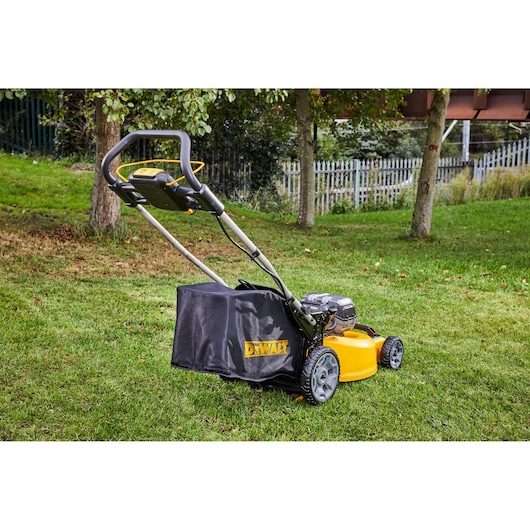 DEWALT cordless lawn mower on grass with a tree and fence in the background.