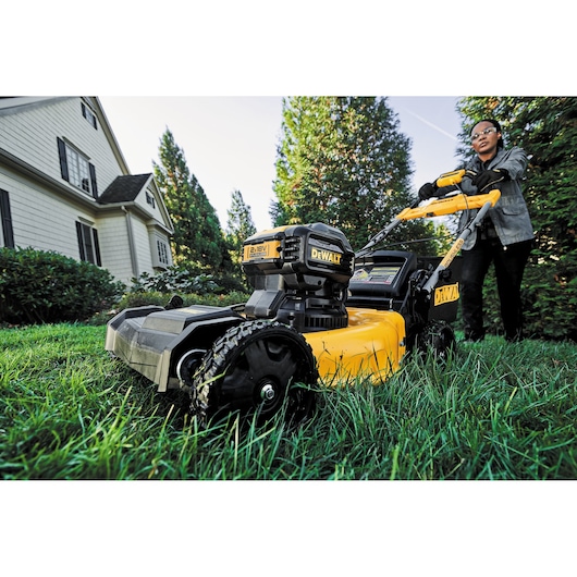 DEWALT lawn mower in use on grass near a house, user blurred for privacy.