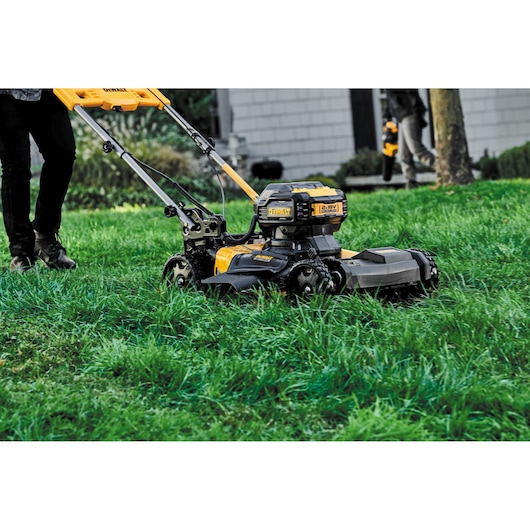 Yellow DEWALT lawn mower in use on green grass outdoors. Person partially visible pushing the mower.